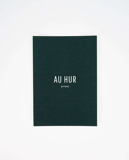 Dunkelgrüne Postkarte mit weißer Aufschrift „AU HUR“ in Großbuchstaben, darunter in kleiner Schrift die phonetische Schreibweise „[ao huːr]“.
