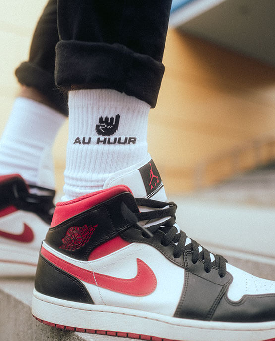 Weiße AU HUUR-Socken mit schwarzem Logo und Handzeichen, getragen mit Nike Air Jordan Sneakern in Schwarz-Weiß-Rot, lässiger Streetstyle-Look im urbanen Umfeld.

