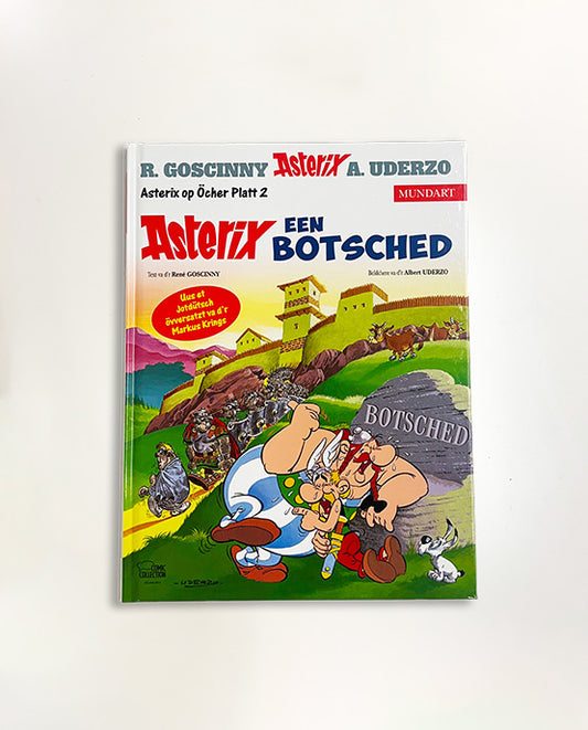 Asterix-Comic „Asterix een Botsched“ auf Öcher Platt (Band 2) mit farbenfrohem Cover, auf dem Asterix und Obelix vor einem gallischen Dorf und römischer Garnison zu sehen sind. Öcher Mundart-Ausgabe, übersetzt von Markus Krings.