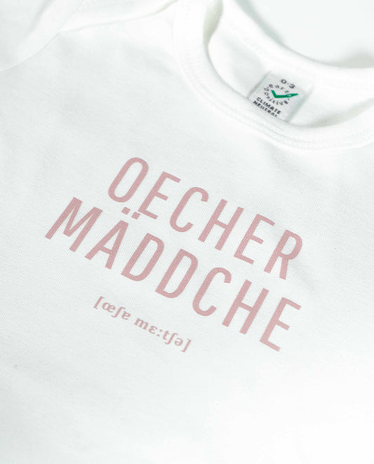 Nahaufnahme des weißen Babybodys mit rosa Aufdruck „Oecher Mäddche“ und Lautschrift darunter. Zeigt Textur des Stoffes und hochwertigen Siebdruck.