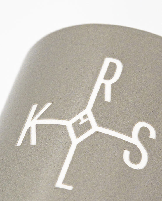 Grauer Keramikbecher im Close-up mit eingeprägtem, weißem KAROLUS (KRLS)-Logo 