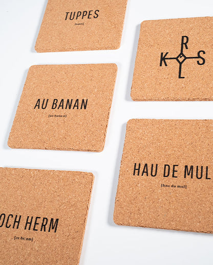 Sechs quadratische Kork-Untersetzer mit Aachener Sprüchen wie „TUPPES“, „AU BANAN“, „KRLS“, „HAU DE MULL“ und „OCH HERM“