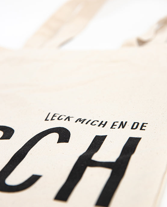 Detailaufnahme des naturfarbenen Jutebeutels mit schwarzem Druck „LECK MICH EN DE TÄSCH“ 