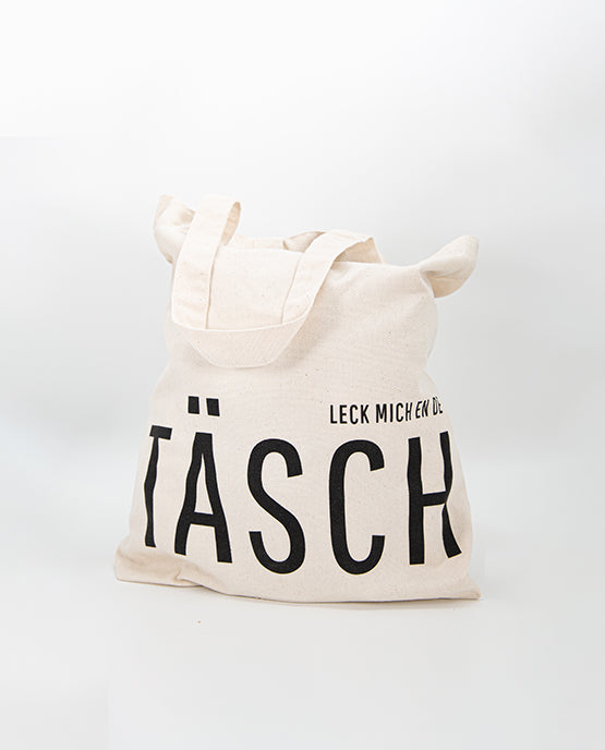 Naturfarbener Jutebeutel mit schwarzem Aufdruck „LECK MICH EN DE TÄSCH“, gefüllt dargestellt – humorvoller Stoffbeutel aus robuster Baumwolle, ideal für Alltag und Einkauf.