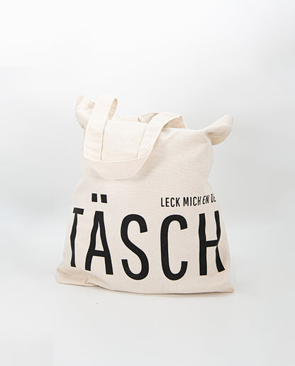 Naturfarbener Jutebeutel mit schwarzem Aufdruck „LECK MICH EN DE TÄSCH“, gefüllt dargestellt – humorvoller Stoffbeutel aus robuster Baumwolle, ideal für Alltag und Einkauf.