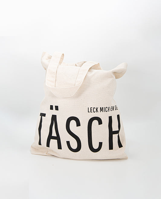 Naturfarbener Jutebeutel mit schwarzem Aufdruck „LECK MICH EN DE TÄSCH“, gefüllt dargestellt – humorvoller Stoffbeutel aus robuster Baumwolle, ideal für Alltag und Einkauf.