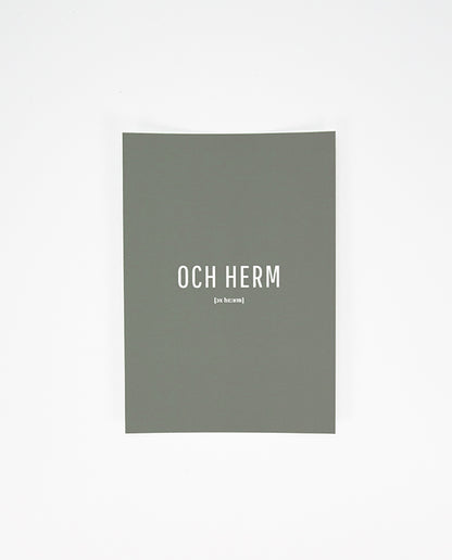 Vorderseite einer grauen Postkarte mit der weißen Aufschrift „OCH HERM“ in Großbuchstaben und der phonetischen Schreibweise „[ɔx hɛ:ʁm]“ darunter.