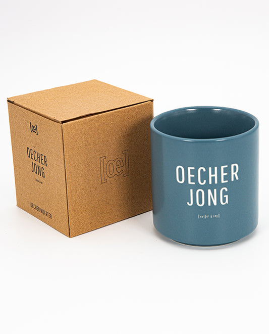 Blauer Keramikbecher „OECHER JONG“ mit Lautschrift, daneben braune [oe]-Verpackung