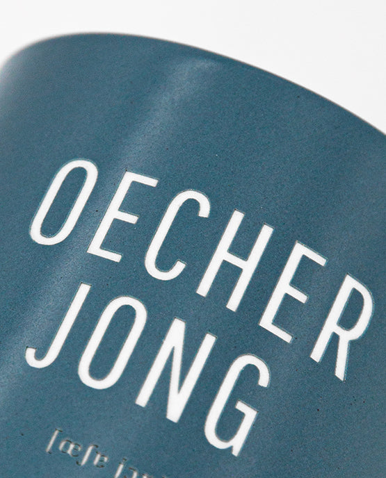 Detailaufnahme eines blauen Keramikbechers mit dem Schriftzug „OECHER JONG“ und phonetischer Lautschrift