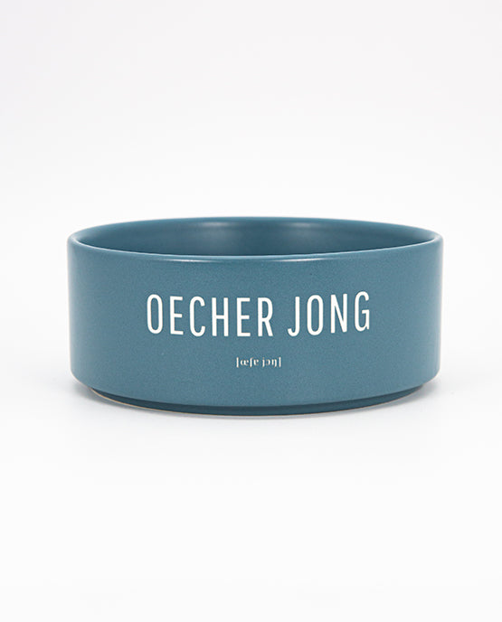 Blauer Keramiknapf mit weißem Schriftzug „OECHER JONG“ und phonetischer Lautschrift auf weißem Hintergrund, zentriert und freigestellt.