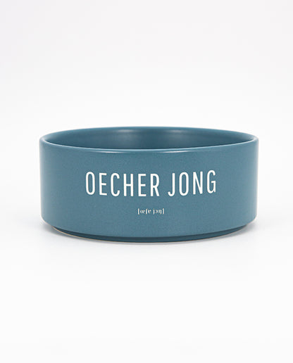 Blauer Keramiknapf mit weißem Schriftzug „OECHER JONG“ und phonetischer Lautschrift auf weißem Hintergrund, zentriert und freigestellt.