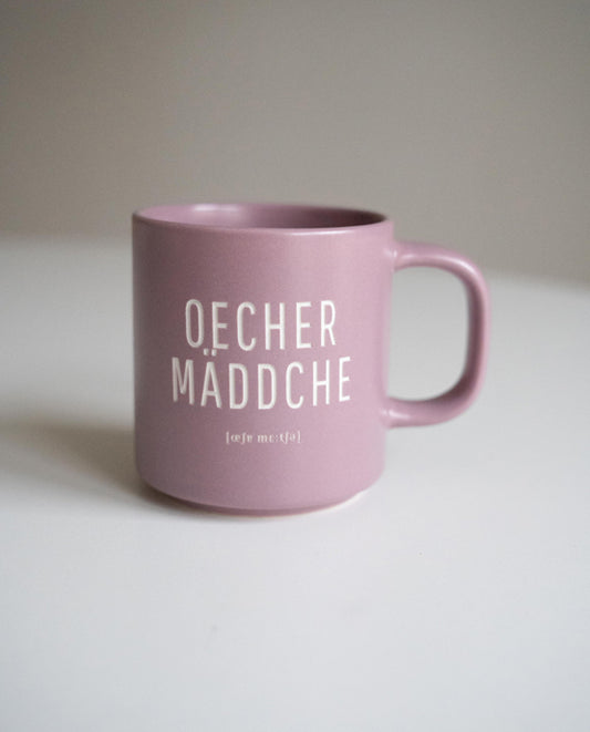 Rosa Keramiktasse mit weißem Aufdruck „OECHER MÄDDCHE“ in Großbuchstaben, fotografiert auf hellem Hintergrund