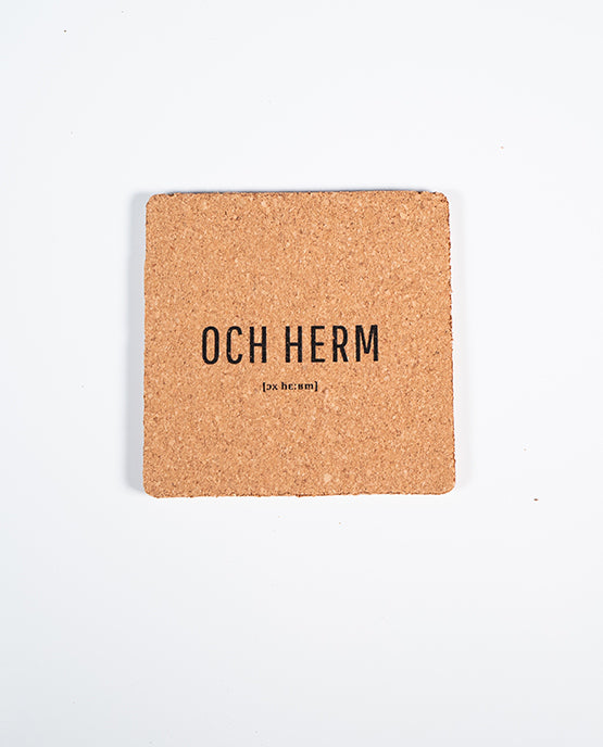 Quadratischer Kork-Untersetzer mit schwarzem Schriftzug „OCH HERM“ und lautsprachlicher Notation [ɔx hɛʁm], fotografiert auf weißem Hintergrund.