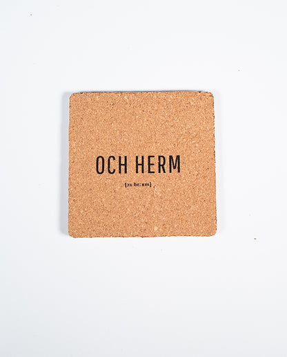 Quadratischer Kork-Untersetzer mit schwarzem Schriftzug „OCH HERM“ und lautsprachlicher Notation [ɔx hɛʁm], fotografiert auf weißem Hintergrund.