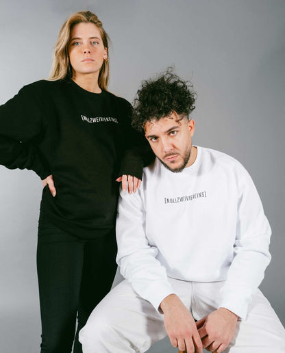 Frau steht in schwarzem Sweatshirt mit weißem Schriftzug „[NULLZWEIVIEREINS]“ und schwarzer Hose, während ein Mann davor sitzt und ein weißes Sweatshirt mit schwarzem Schriftzug „[NULLZWEIVIEREINS]“ sowie weiße Hose trägt. Beide posieren vor grauem Hintergrund.