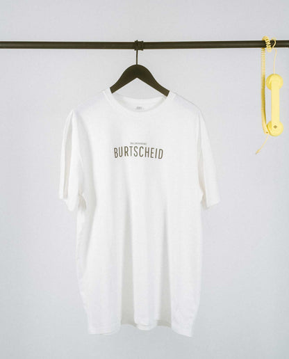 Weißes T-Shirt mit Typografie: Mittig auf der Brust steht in großen schwarzen Buchstaben „BURTSCHEID“. Direkt darüber ist in kleinerer Schrift [NULLZWEIVIEREINS] platziert, die die Aachener Vorwahl widerspiegelt. Das schlichte, klare Design macht das Shirt zu einem modernen Statement-Piece für alle, die ihre Verbundenheit zu Burtscheid zeigen möchten.