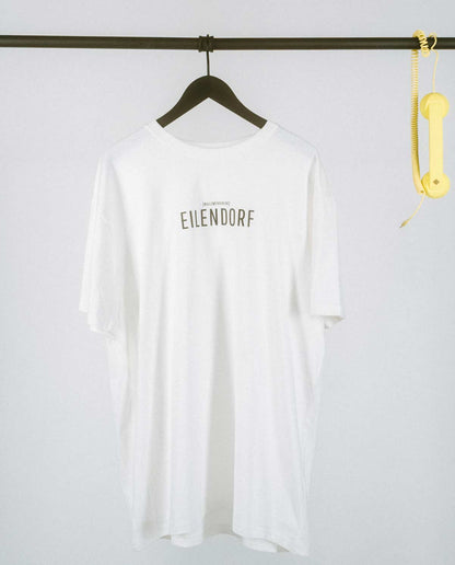 Weißes T-Shirt mit dem Schriftzug „EILENDORF“ in schlichten, schwarzen Großbuchstaben, mittig auf der Brust. Über dem Ortsnamen steht in kleinerer Schrift die Lautschrift [nʏlʦvaɪfɪaɪns], was dem Aachener Postleitzahlenbereich entspricht. Das minimalistische Design hebt den Stadtteil Eilendorf stilvoll hervor und sorgt für einen modernen, urbanen Look.