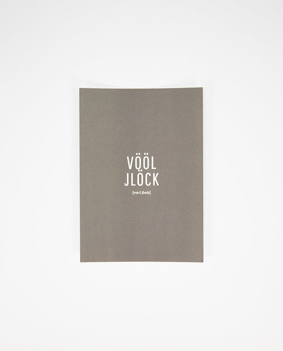 Graue Postkarte mit weißem Aufdruck in der Mitte: „VÖÖL JLÖCK“ in Großbuchstaben, darunter in kleinerer Schrift die Lautschrift.